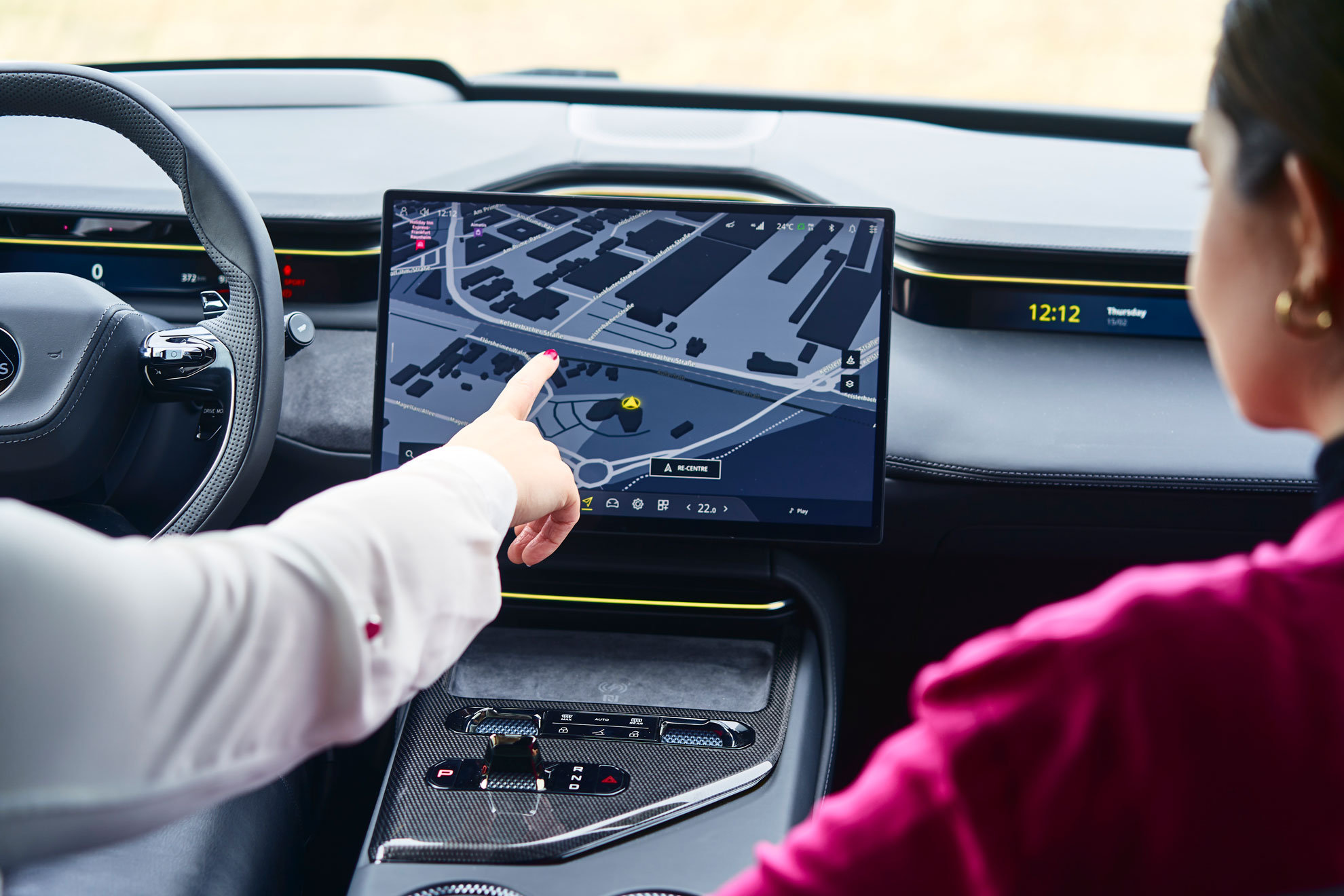 Bildschirm innerhalb eines Fahrzeugs auf dem ein Navigationsprogramm zu sehen ist. Man sieht, wie die Fahrerin des Autos darauf zeigt. Die Beifahrerin ist ebenfalls von hinten im Anschnitt zu sehen und blickt auf den Monitor.