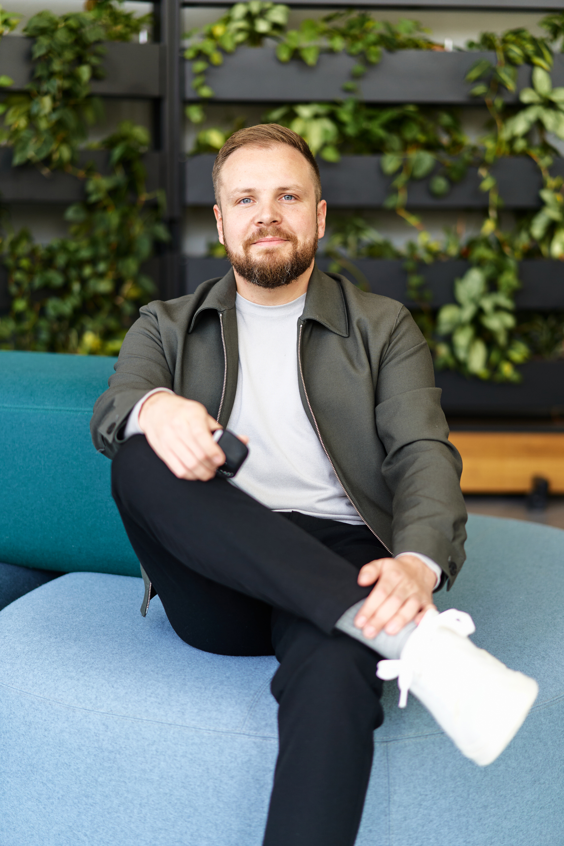 Ein Mann sitzt entspannt auf einem blauen Sofa in einem modernen Raum mit Pflanzen im Hintergrund.