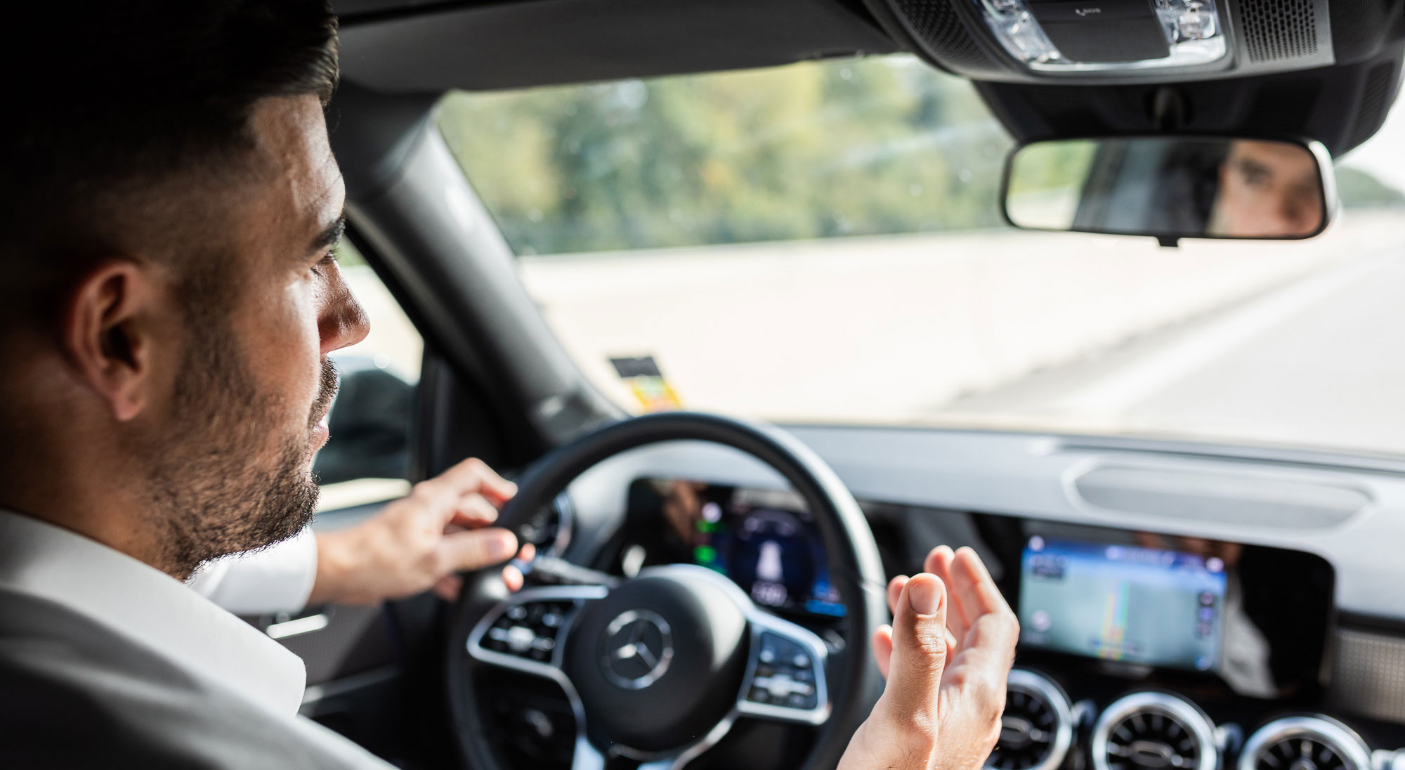 Felix Küster sitzt in seinem Auto. Eine Hand am Lenkrad, die andere im Gespräch über die Fernsprechanlage gehoben. 