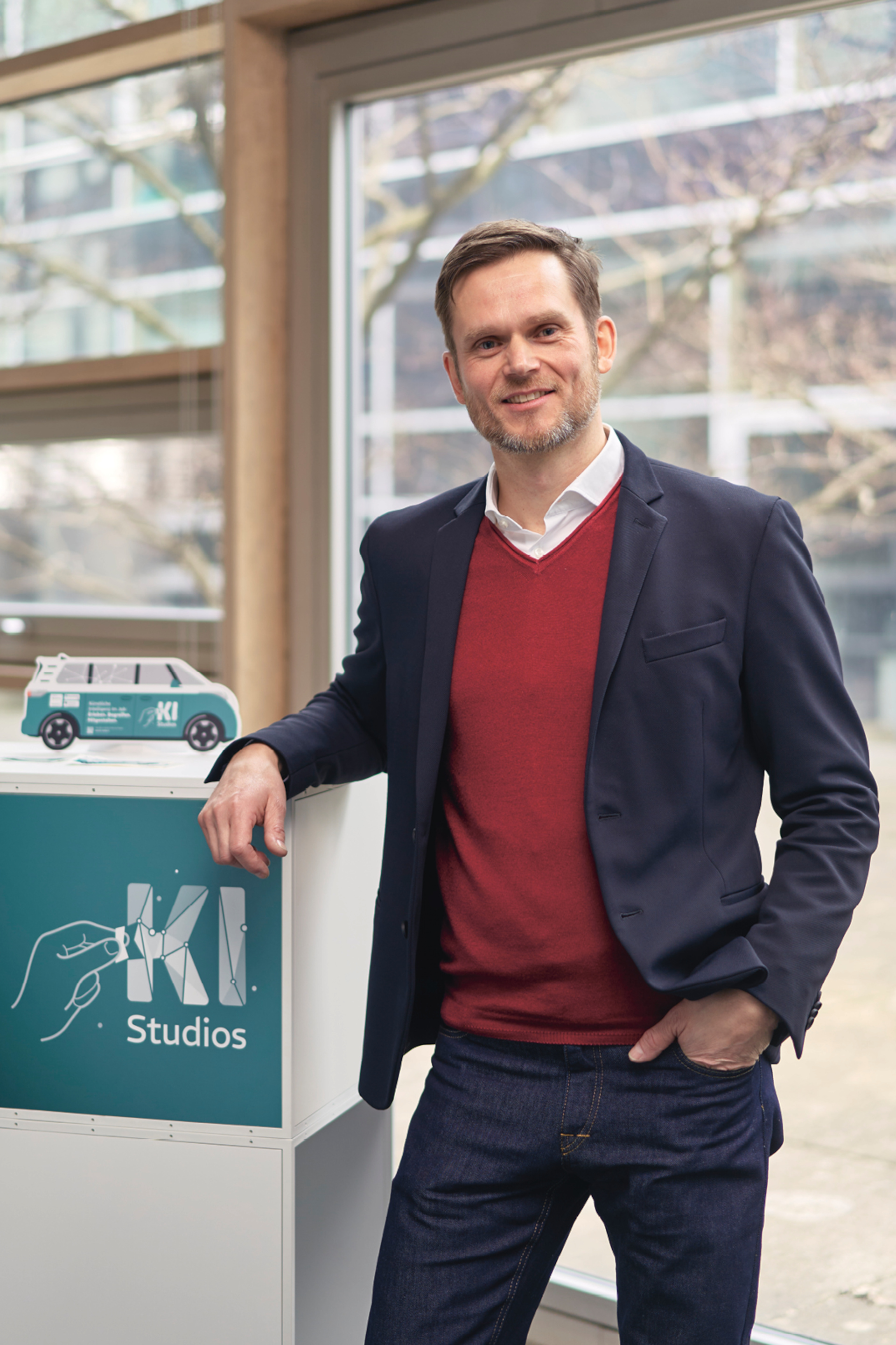 Dr. Matthias Peissner lehnt an einem brusthohen Regal mit der Aufschrift "KI-Studios" und blickt lächelnd in die Kamera. .