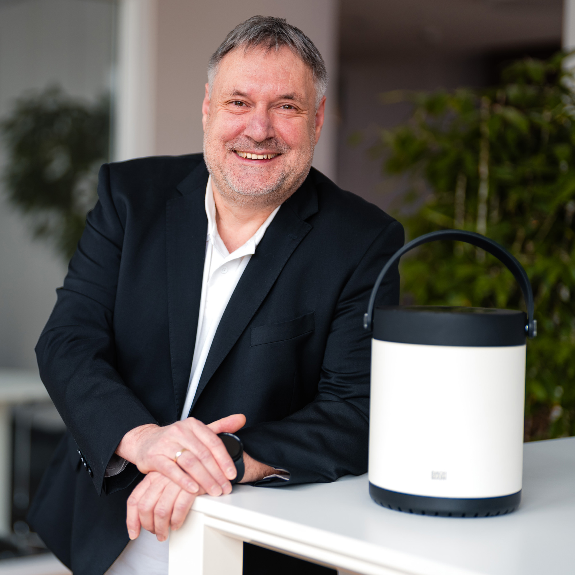 Günter Schnieder lehnt locker an einem Tisch und blickt lächelnd in die Kamera. Neben ihm auf dem Tisch steht die MOV:E.