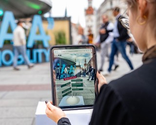 Eine Person betrachtet auf einem Tablet eine Aufnahme eines Stadtbildes, das von der Tablet-Kamera festgehalten wird. Das Tablet fügt zusätzliche örtliche Informationen ein.