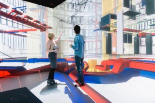Zwei Personen diskutieren vor einer digitalen Visualisierung eines Gebäudemodells mit farblich hervorgehobenen technischen Anlagen – Symbolbild für digitale Planung, BIM und innovative Technologien im industrialisierten Bauen.