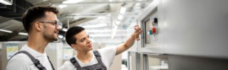 Erfahrener Techniker, der neue Mitarbeiter in der Bedienung von Industriemaschinen in der Fabrik schult.