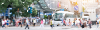 Stadtausschnitt mit Personen, die über einen Zebrastreifen laufen, einer Straße mit öffentlichem Verkehr und einem Bus, umgeben von begrünten Gebäuden. Über das Bild ist ein abstraktes Netzsystem eingearbeitet.